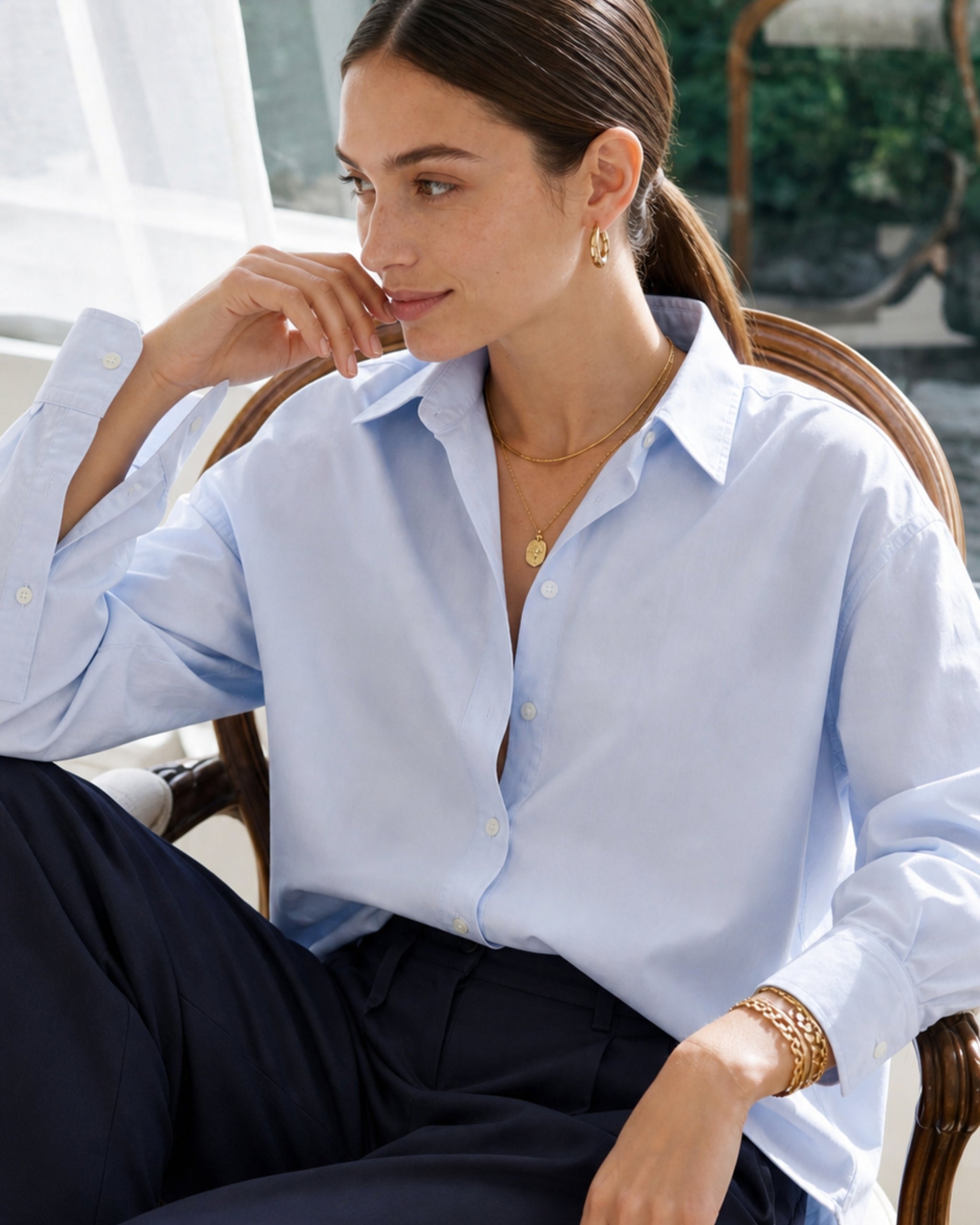 Vrouw in poplin shirt in lichtblauw zittend bij een zonverlicht raam