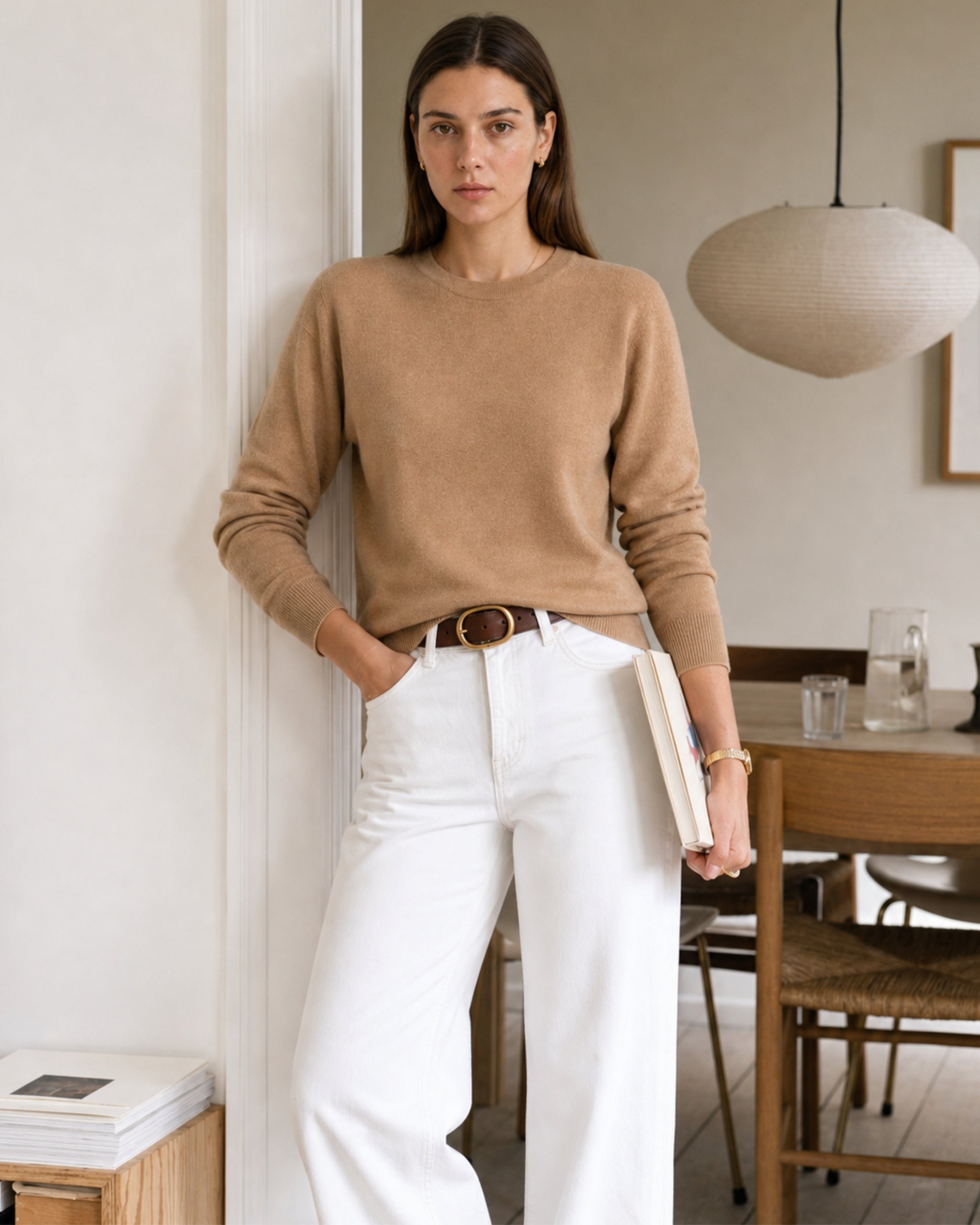 Vrouw in merinotrui in camel en wit jeans houdt een boek vast thuis